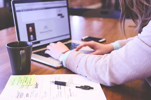 Woman typing at a laptop with business documents at her side.