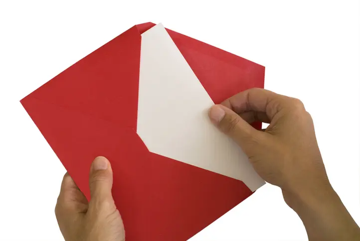 Hands removing a solid white note from a red envelope. Sending a red letter to unresponsive clients can get a quick, concrete response.