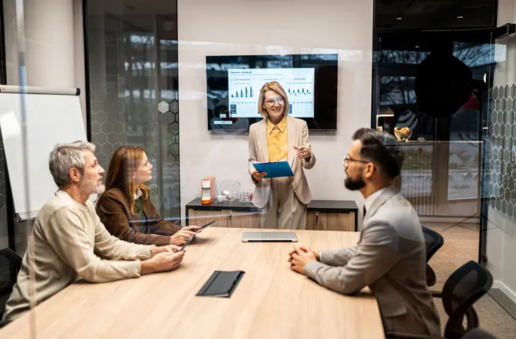 An advisor giving a presentation to a group seated at a table. Relatable stories are more reliable than abstract advice.