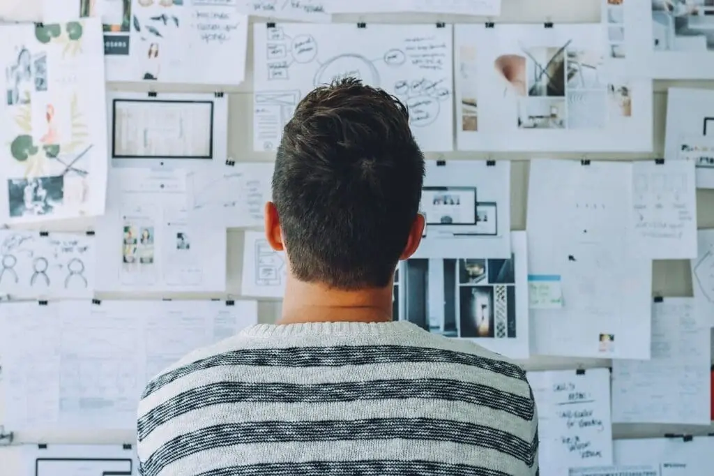 A man staring at a wall covered in paper diagrams. Starting a conversation today creates opportunities for a better porfolio.